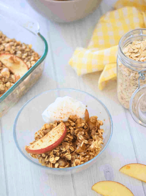 Warm apple crisp made with oats and cinnamon, served in a glass bowl with whipped topping—one of the coziest things to make with apples and a must-try for easy fall recipes.