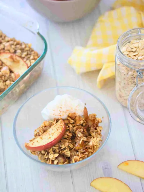 Warm apple crisp made with oats and cinnamon, served in a glass bowl with whipped topping—one of the coziest things to make with apples and a must-try for easy fall recipes.