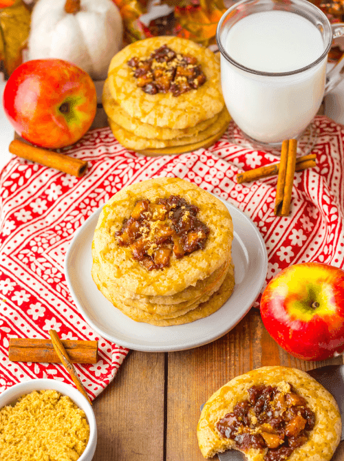 Apple pie cookies with a gooey apple filling and golden crumble topping, stacked beside a glass of milk on a red fall napkin – festive and simple fall treats, perfect things to make with apples.
