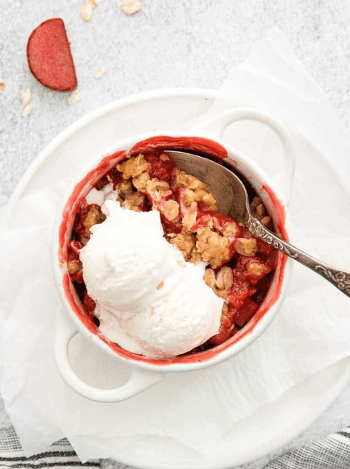 Mini apple strawberry crisp topped with vanilla ice cream in a white ramekin—one of the most colorful fall desserts and a fresh, fruity twist on things to make with apples.