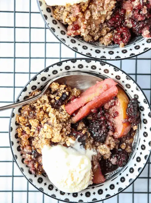 Apple and blackberry crumble with oats and vanilla ice cream in a patterned bowl—one of the most colorful fall desserts and a cozy, fruit-filled option when looking for things to make with apples.