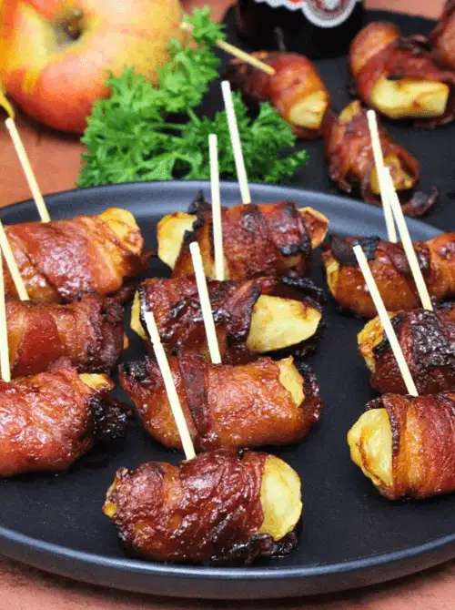 Bacon-wrapped apple bites secured with toothpicks on a black plate—sweet, savory, and perfect for party appetizers or easy fall recipes when you need fun things to make with apples.