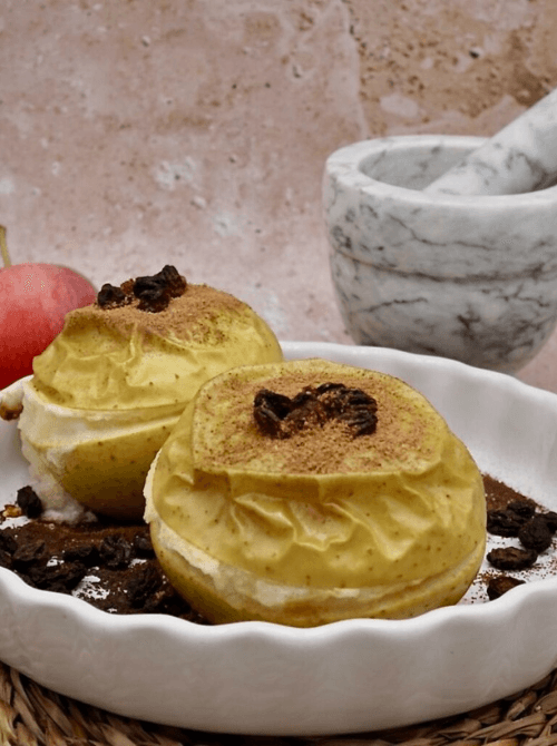 Whole baked apples filled with a creamy center and topped with raisins and cinnamon—served in a white dish for a rustic, cozy fall dessert presentation.