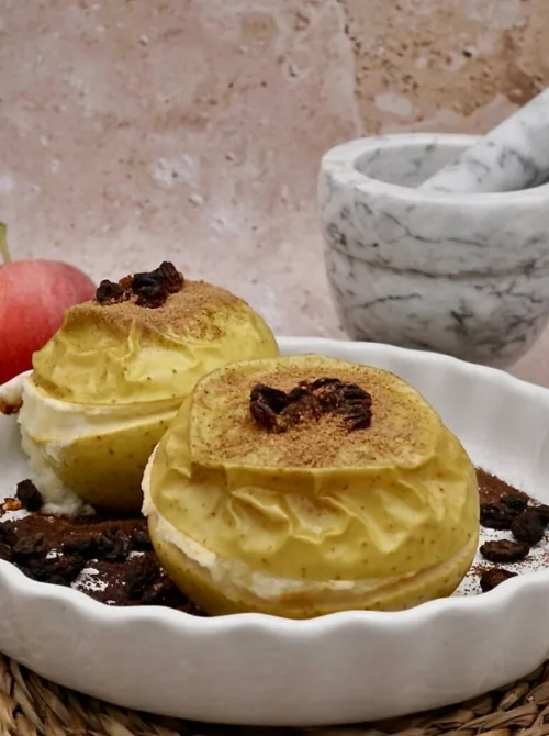 Whole baked apples filled with a creamy center and topped with raisins and cinnamon—served in a white dish for a rustic, cozy fall dessert presentation.