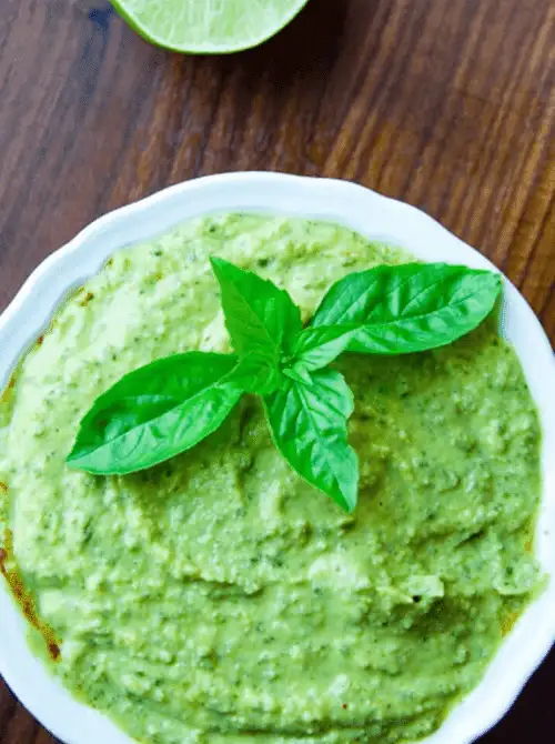 Creamy green dip topped with fresh basil leaves, served in a white bowl—an eye-catching addition to any spread of easy game day dips.