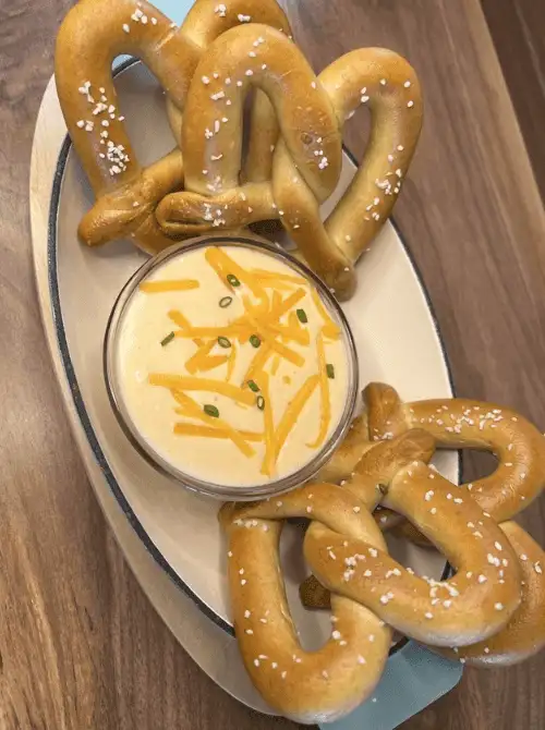 Soft pretzels served with cheddar nacho cheese sauce in a glass bowl—an easy and crowd-pleasing option for football party snacks on a budget.