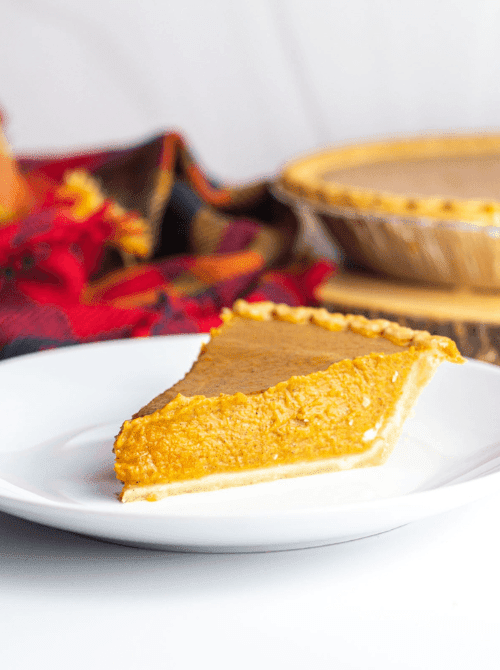 A single slice of classic pumpkin pie on a white plate with a plaid fall napkin in the background—an easy, nostalgic dessert idea for using up leftover pumpkin puree.