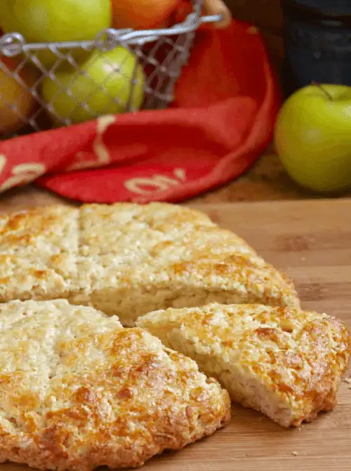 Golden British apple scones freshly baked and sliced on a wooden board, with apples in the background—an easy idea for what to make with apples and a cozy fall bread recipe.