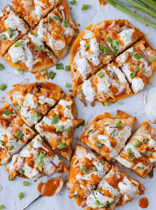 Mini buffalo chicken naan pizzas drizzled with ranch and sprinkled with green onions—an easy, flavor-packed option for football party snacks on a budget.