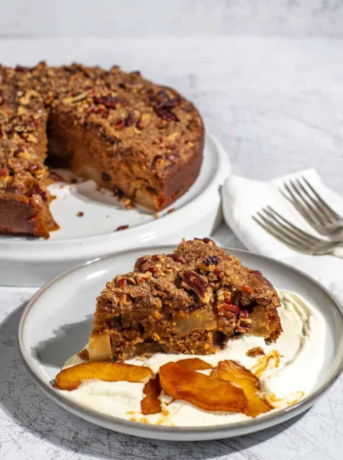 Slice of spiced apple cake topped with pecan crumble and served with whipped cream and caramelized apples—one of the most rustic and flavor-packed fall desserts, and a delicious option when looking for things to make with apples.