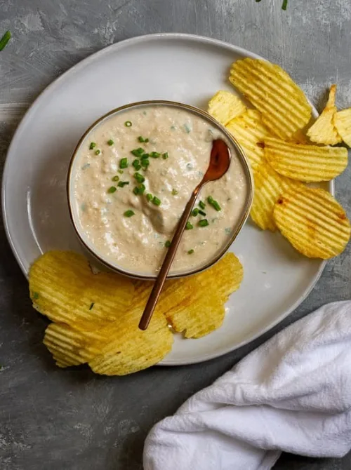 Bowl of creamy onion dip garnished with chives and surrounded by ridged potato chips, making it one of the best easy game day dips for snacking.