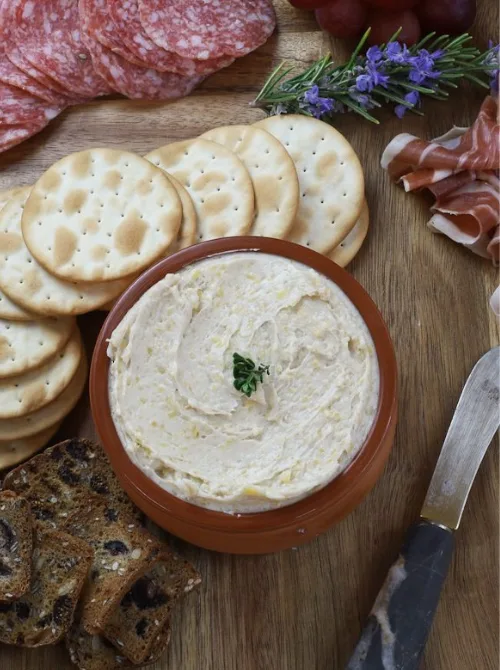 Creamy cheese spread served in a brown bowl with crackers, salami, and prosciutto—budget-friendly tailgate food idea perfect for feeding a crowd.