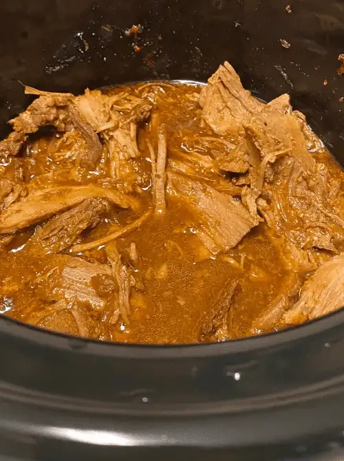 Tender pulled pork simmering in a slow cooker with rich sauce—an easy tailgate food option on a budget that’s perfect for feeding a crowd.
