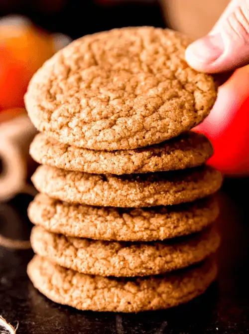 Stack of soft apple spice cookies with a hand reaching for the top – cozy, simple fall treats and one of the easiest things to make with apples for autumn baking.