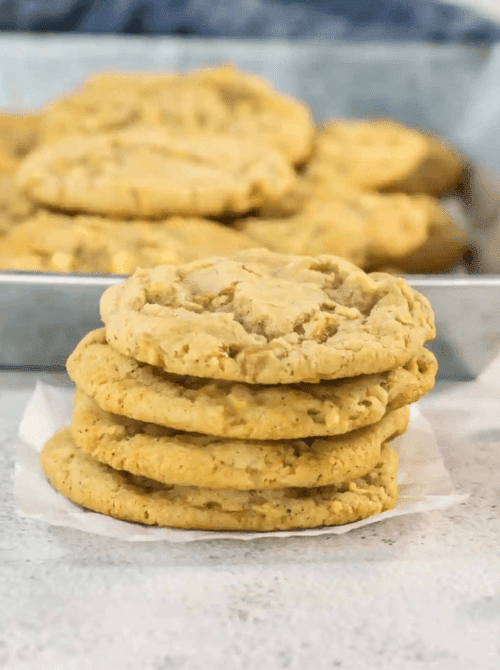 Stack of chewy caramel apple cookies with more cooling in the background – one of the easiest things to make with apples and a deliciously simple fall treat.