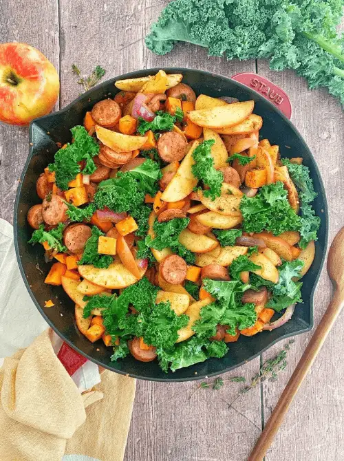 Colorful skillet with sautéed apples, smoked sausage, sweet potatoes, red onions, and kale—an easy fall recipe and a flavorful way to use up apples in hearty weeknight meals.