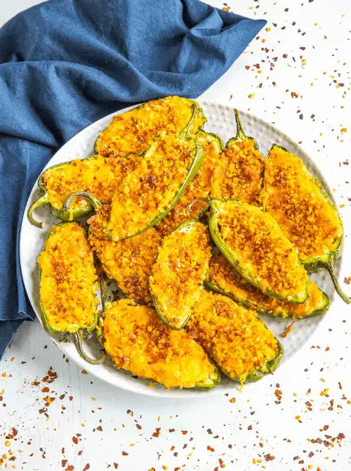 Baked jalapeño poppers stuffed with cheese and topped with a crispy golden crust, served on a white plate—an easy and spicy favorite for football party snacks on a budget.