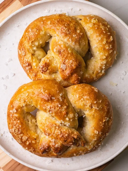 Golden-brown homemade soft pretzels topped with coarse salt, served on a neutral ceramic plate—an easy and hearty option for football party snacks on a budget.