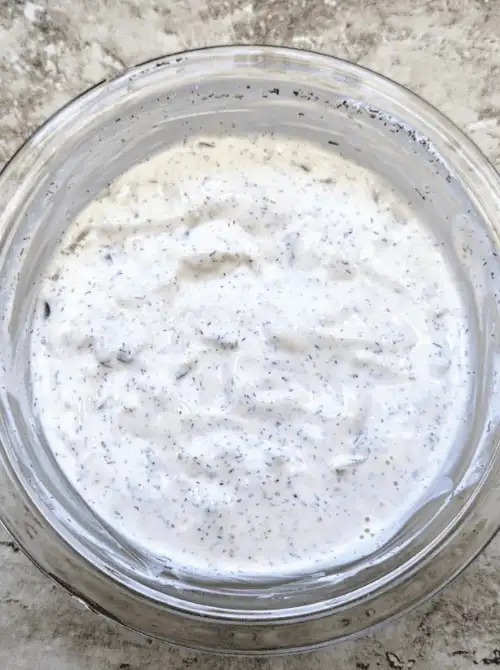 A glass bowl filled with creamy dill pickle dip, a tangy and refreshing option for your easy game day dips spread.