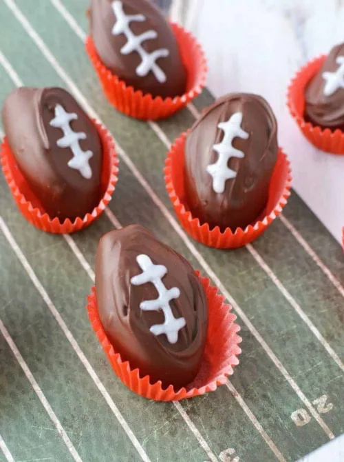 Individual chocolate dessert cups layered with crushed cookies and pudding, topped with green frosting “grass” and a chocolate-covered football cookie—perfect for football party snacks on a budget that look festive and fun without breaking the bank.