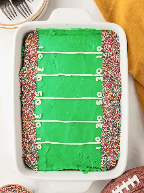Football field cake decorated with bright green frosting, yard lines, and colorful sprinkles—an easy, festive dessert perfect for football party snacks on a budget.