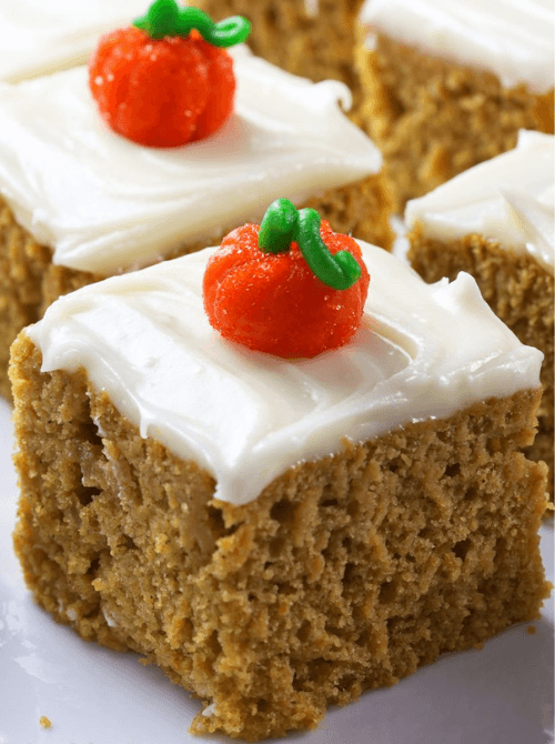Moist pumpkin cake squares topped with creamy white frosting and festive candy pumpkins—an adorable and tasty idea for what to make with leftover pumpkin puree in pumpkin cakes and cupcakes.