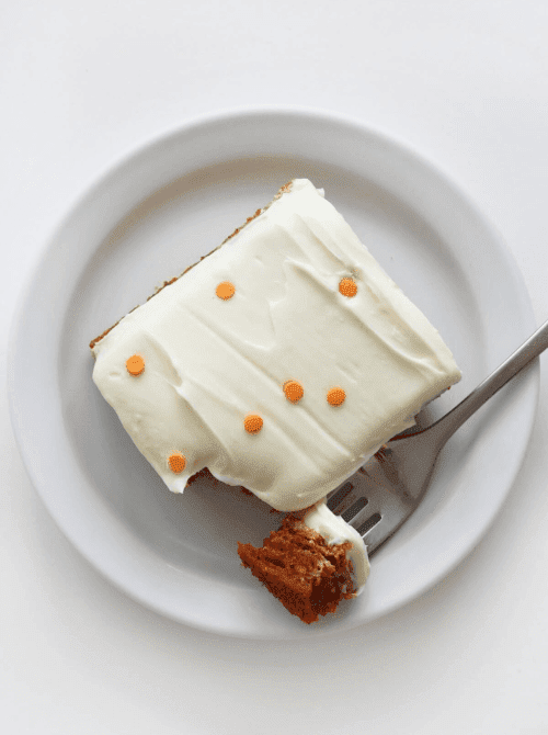 A slice of moist pumpkin cake topped with creamy white frosting and orange sprinkles, showcasing an easy idea for what to make with leftover pumpkin puree in pumpkin cakes and cupcakes.