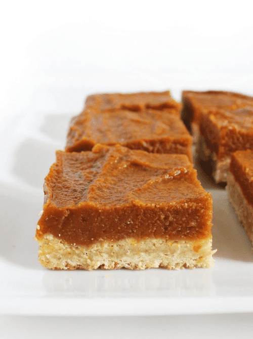 Pumpkin pie bars with a thick spiced filling and golden oat crust, neatly arranged on a white platter—an easy, mess-free option for what to do with leftover pumpkin puree.