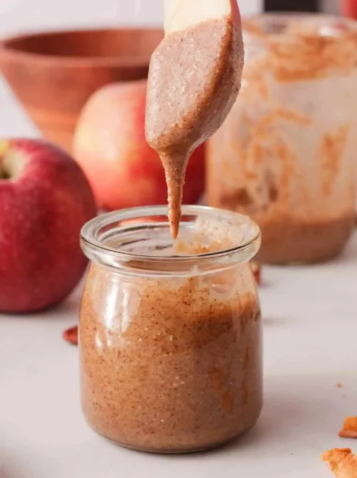 Creamy homemade apple pecan butter in a glass jar with a fresh apple slice dipped in—perfect for snack boards or spreads when looking for easy fall recipes and creative things to make with apples.