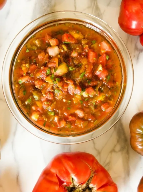 Fresh tomato salsa in a glass bowl surrounded by heirloom tomatoes, perfect for topping chips or tacos—one of the must-have easy game day dips.