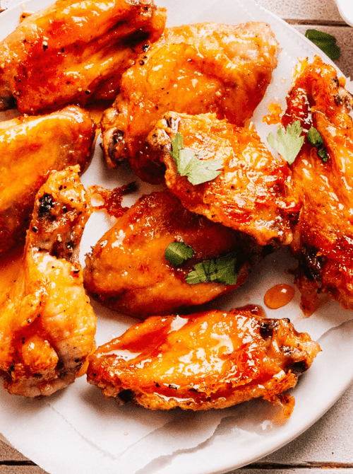 Buffalo chicken wings coated in spicy sauce and garnished with parsley—classic tailgate food on a budget that's perfect for feeding a hungry crowd.