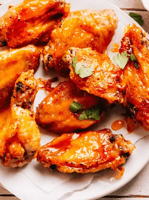 Buffalo chicken wings coated in spicy sauce and garnished with parsley—classic tailgate food on a budget that's perfect for feeding a hungry crowd.