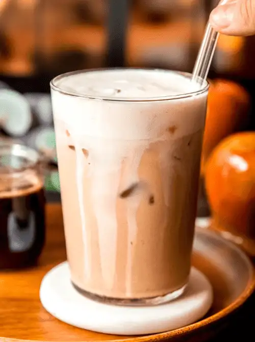 Iced apple crisp latte in a tall glass with creamy foam and a straw—smooth, spiced, and a cozy coffeehouse-inspired drink that’s perfect for easy fall recipes and delicious things to make with apples.