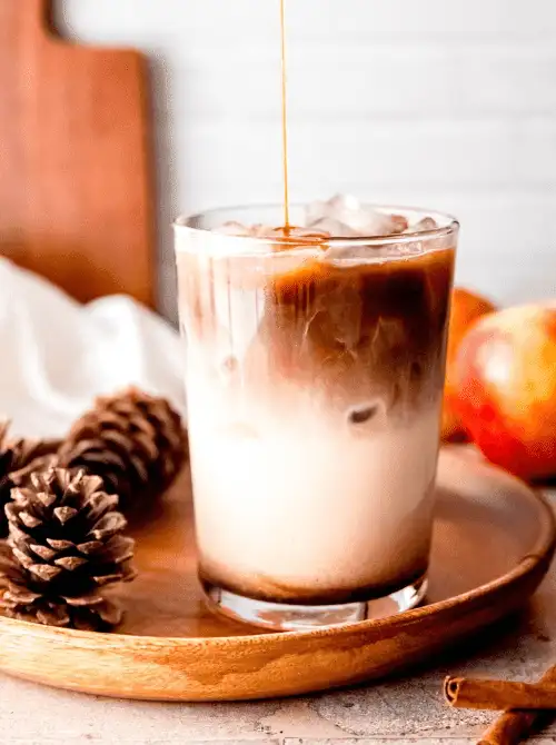 Iced apple crisp macchiato in a clear glass with espresso being poured over milk and ice—layered, spiced, and one of the coziest things to make with apples for easy fall recipes and homemade coffee lovers.