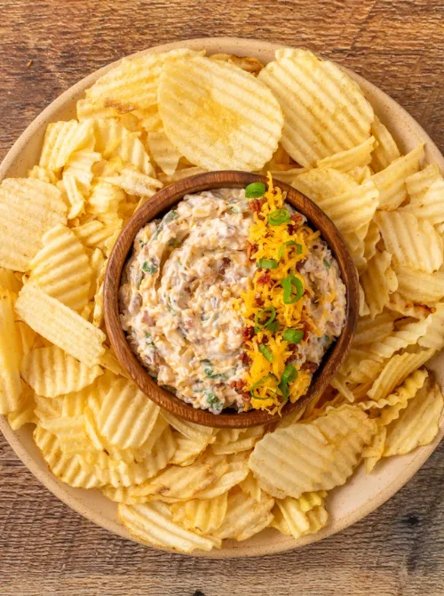 Loaded bacon cheddar ranch dip served in a wooden bowl surrounded by ridged potato chips—an irresistible and budget-friendly choice for football party snacks on a budget.