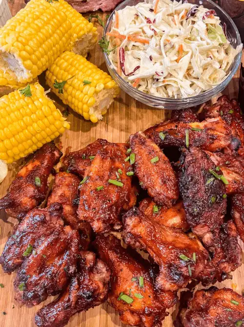 Maple Bourbon chicken wings served with corn on the cob and creamy coleslaw on a wooden platter—flavor-packed tailgate food on a budget that’s perfect for feeding a crowd.