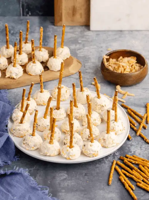 Mini cheese balls with pretzel stick handles arranged on white and wooden serving trays—an easy, mess-free appetizer perfect for football party snacks on a budget.