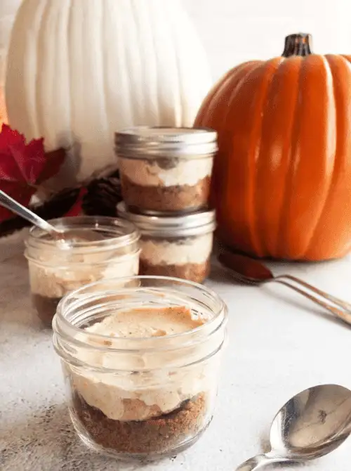 Mini no-bake pumpkin cheesecakes layered in glass jars with graham cracker crust, perfect for fall gatherings — a fun and easy pumpkin cheesecake recipe to use up leftover pumpkin purée.