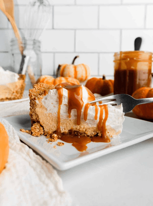 Slice of no-bake pumpkin cheesecake topped with whipped cream and drizzled with caramel sauce, served on a white plate with mini pumpkins in the background—a rich, no-fuss dessert idea for using leftover pumpkin puree.