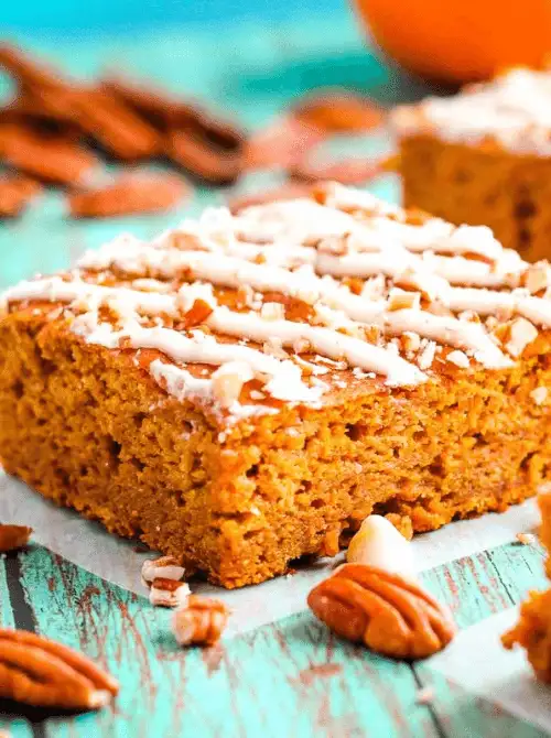 Moist pumpkin bar topped with icing drizzle and chopped pecans on a rustic turquoise surface—an easy and flavorful pumpkin dessert made with leftover pumpkin puree.