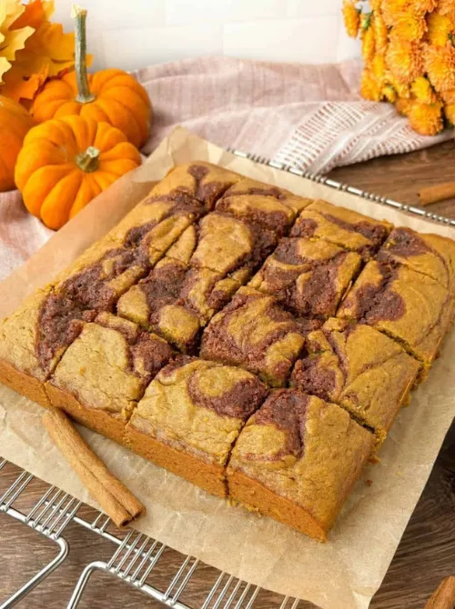 Pumpkin blondies with a cinnamon swirl pattern, sliced into squares and displayed on parchment paper—an inviting fall treat and clever way to use up leftover pumpkin puree in a dessert.