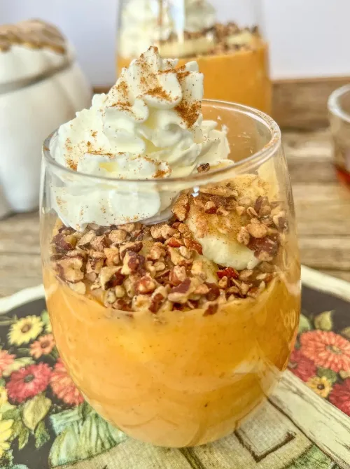 Pumpkin cheesecake pudding layered in a glass with chopped pecans, banana slices, and whipped cream — a light, no-bake fall dessert that’s perfect for using up leftover pumpkin purée.