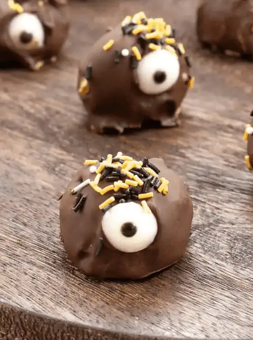 Chocolate-covered Halloween truffle decorated like a monster with candy eyes and orange-and-black sprinkles — a fun and festive no-bake dessert idea for leftover pumpkin purée or easy pumpkin cheesecake filling.