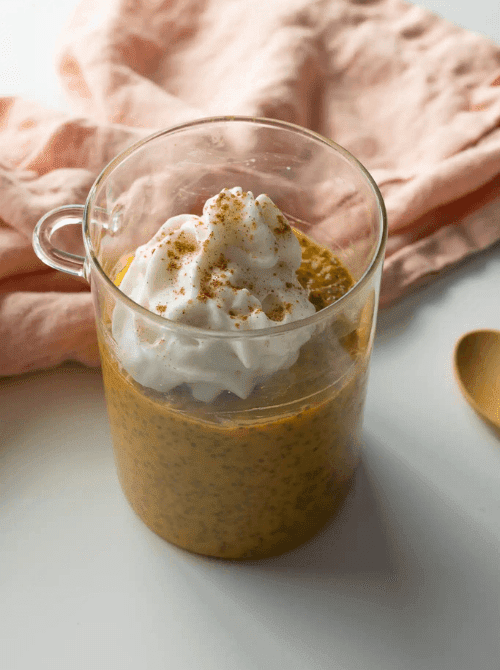 Glass mug of pumpkin chia pudding topped with whipped cream and cinnamon—an easy, healthy pumpkin dessert and creative way to use leftover pumpkin puree.