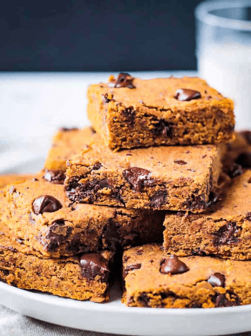 Stack of vegan pumpkin chocolate chip bars on a white plate, filled with gooey chocolate chunks—an allergy-friendly pumpkin dessert and a smart way to use leftover pumpkin puree.