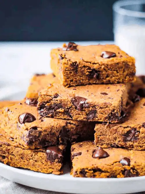 Stack of vegan pumpkin chocolate chip bars on a white plate, filled with gooey chocolate chunks—an allergy-friendly pumpkin dessert and a smart way to use leftover pumpkin puree.