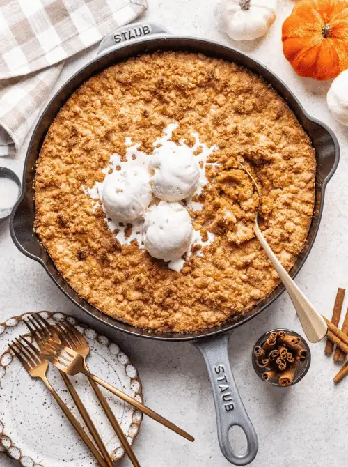 Pumpkin crisp baked in a cast iron skillet, topped with scoops of vanilla ice cream and served with golden forks—a warm, comforting pumpkin dessert and a delicious way to use leftover pumpkin puree.