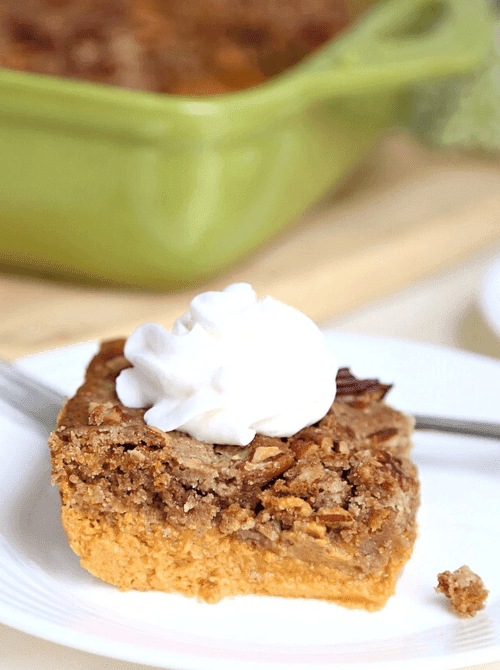 Pumpkin dump cake topped with pecans and whipped cream, served on a white plate—an easy, crowd-pleasing answer for what to make with leftover pumpkin puree using cozy pumpkin cakes and cupcakes.
