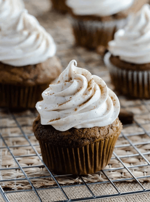 A moist pumpkin cupcake topped with a tall swirl of cinnamon-dusted frosting, cooling on a wire rack—perfect inspiration for what to make with leftover pumpkin puree and delicious pumpkin cakes and cupcakes.