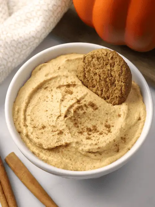 Pumpkin dip topped with cinnamon and served with a gingersnap cookie in a white bowl—an easy fall dessert and delicious way to use up leftover pumpkin puree.